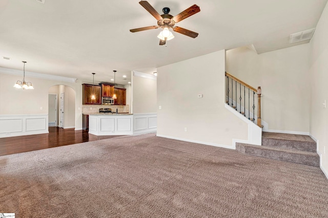 unfurnished living room featuring stairway, a ceiling fan, visible vents, dark carpet, and arched walkways