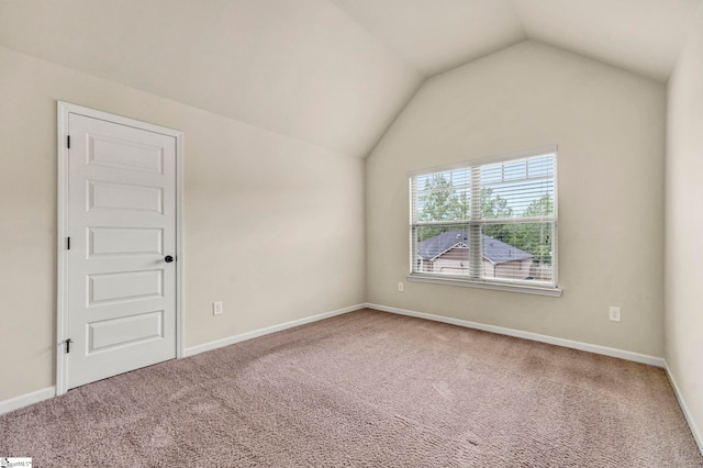 carpeted empty room with vaulted ceiling and baseboards