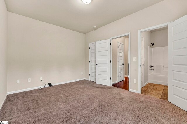 unfurnished bedroom featuring ensuite bath, carpet flooring, and baseboards