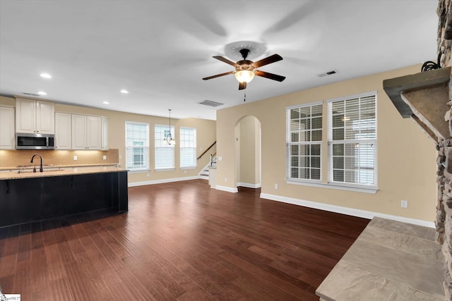 unfurnished living room featuring stairway, visible vents, ceiling fan, baseboards, and arched walkways