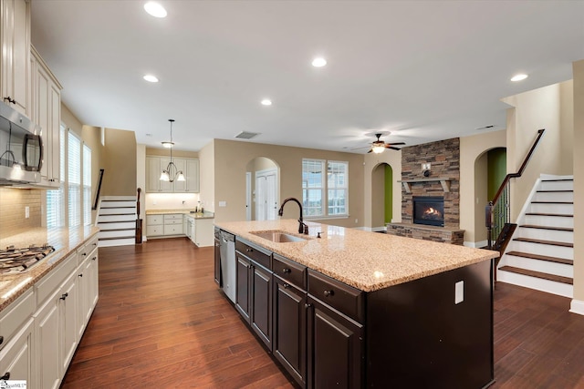 kitchen featuring arched walkways, appliances with stainless steel finishes, a stone fireplace, a sink, and a ceiling fan