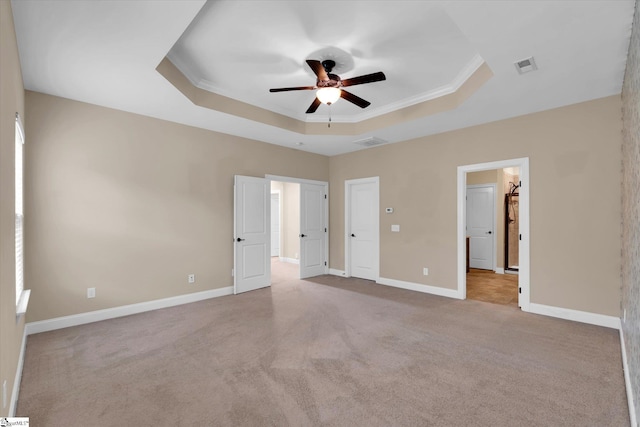 unfurnished bedroom featuring a raised ceiling, visible vents, baseboards, carpet floors, and ornamental molding