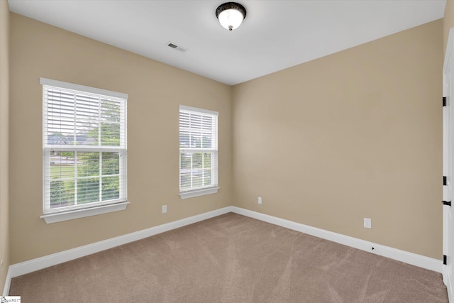 carpeted spare room with visible vents, baseboards, and plenty of natural light