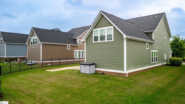 rear view of house featuring fence, roof with shingles, and a lawn