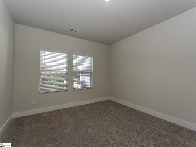spare room featuring baseboards, visible vents, and dark colored carpet