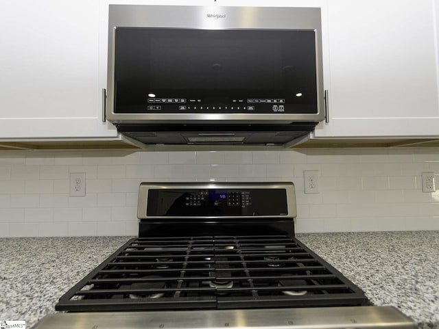 interior details with range with gas stovetop, stainless steel microwave, light stone countertops, tasteful backsplash, and white cabinets