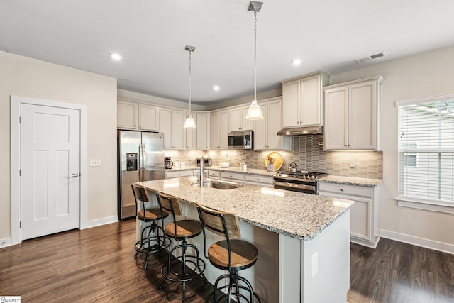 kitchen with under cabinet range hood, appliances with stainless steel finishes, dark wood-style flooring, a sink, and baseboards