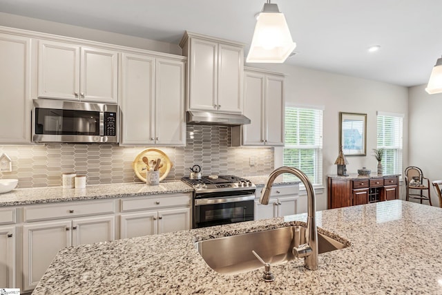 kitchen featuring tasteful backsplash, stainless steel appliances, under cabinet range hood, and a sink
