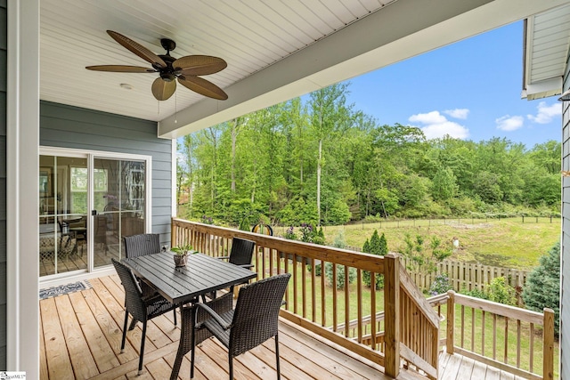 wooden deck with outdoor dining space, a ceiling fan, and a forest view