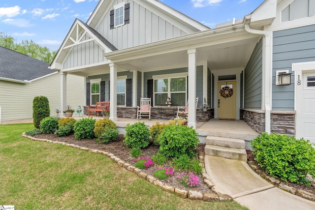 doorway to property featuring a lawn, covered porch, stone siding, and board and batten siding