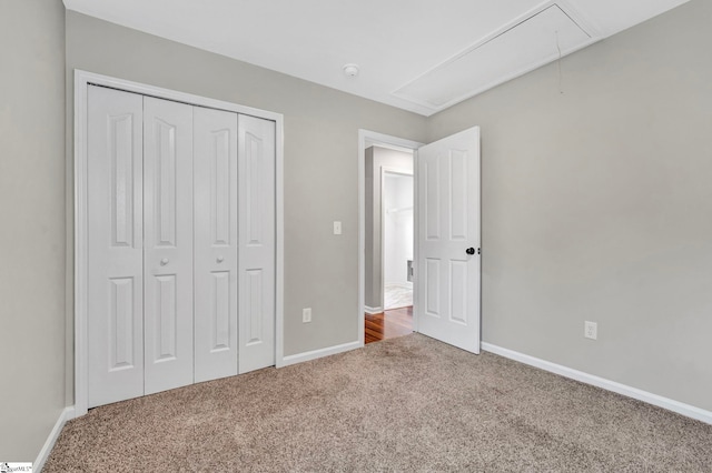 unfurnished bedroom with baseboards, attic access, a closet, and carpet