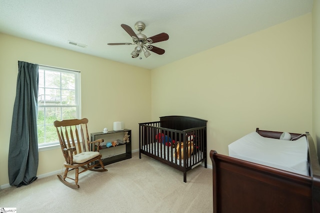 bedroom featuring light colored carpet, visible vents, ceiling fan, a crib, and baseboards