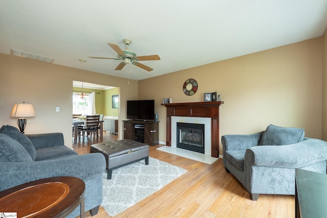 living area featuring light wood-style flooring, visible vents, baseboards, a glass covered fireplace, and a ceiling fan