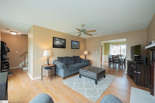 living area featuring stairs, visible vents, light wood-style flooring, and ceiling fan with notable chandelier