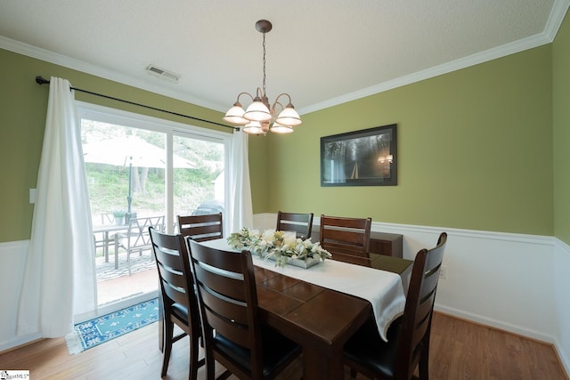 dining room with wood finished floors, visible vents, crown molding, and a notable chandelier