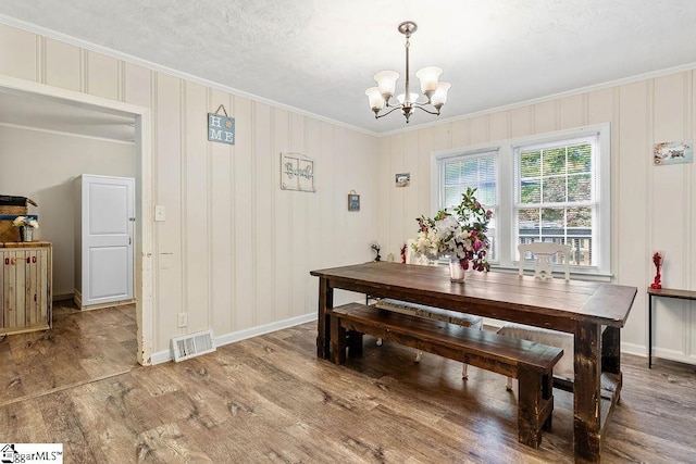 dining area with a notable chandelier, visible vents, baseboards, ornamental molding, and wood finished floors