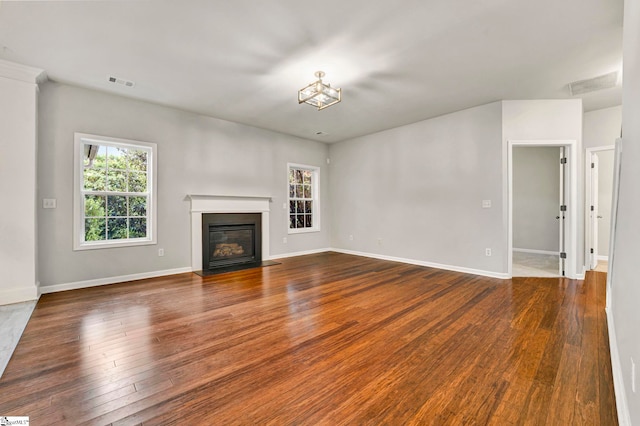 unfurnished living room with visible vents, baseboards, hardwood / wood-style floors, and a glass covered fireplace