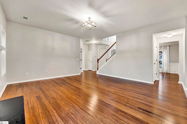 unfurnished living room with stairs, visible vents, hardwood / wood-style flooring, and baseboards