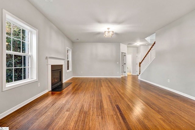 unfurnished living room with stairway, wood finished floors, a glass covered fireplace, and baseboards