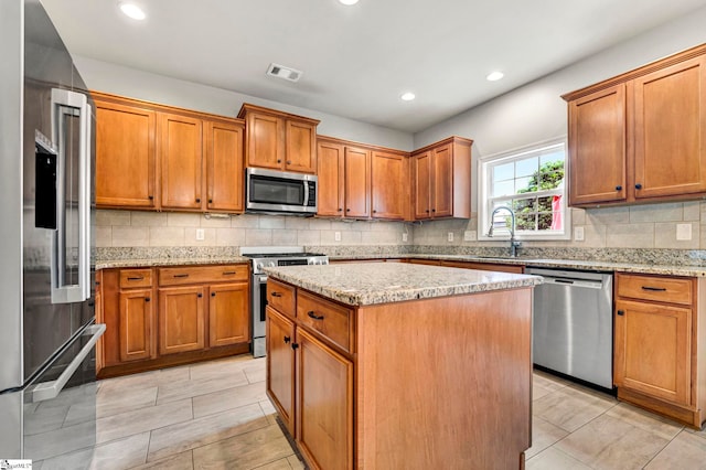 kitchen with brown cabinets, a sink, premium appliances, a center island, and visible vents