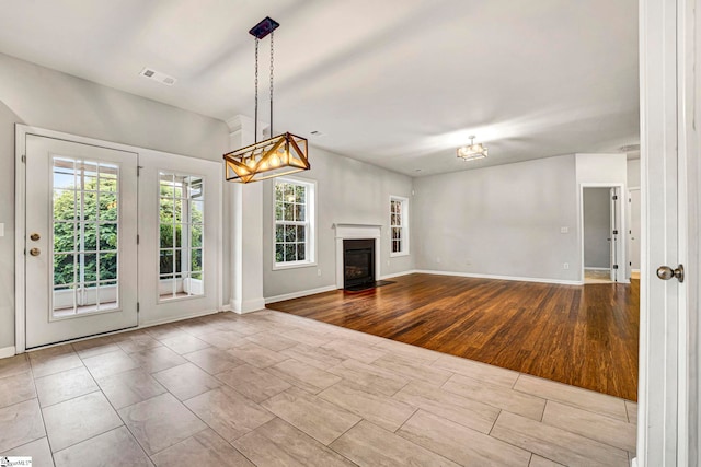 unfurnished living room with a chandelier, a glass covered fireplace, visible vents, baseboards, and wood finished floors