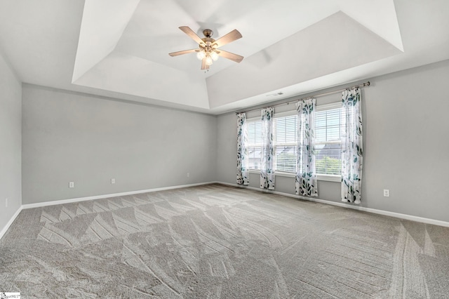 empty room with a raised ceiling, a ceiling fan, carpet flooring, and baseboards