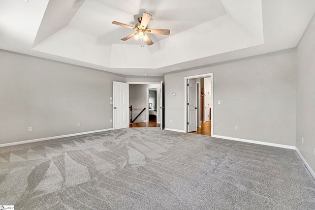 unfurnished bedroom with baseboards, a ceiling fan, carpet floors, and a tray ceiling
