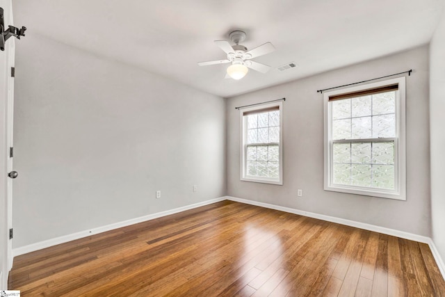 empty room with hardwood / wood-style floors, visible vents, a ceiling fan, and baseboards