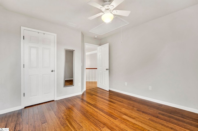 unfurnished bedroom featuring attic access, wood finished floors, a ceiling fan, and baseboards