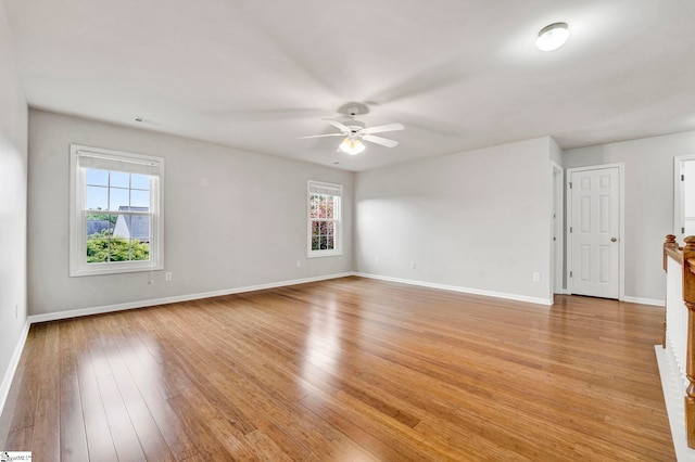 empty room with baseboards, ceiling fan, light wood finished floors, and plenty of natural light