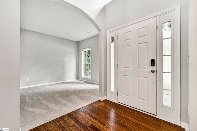 entrance foyer with dark colored carpet, visible vents, baseboards, arched walkways, and dark wood finished floors