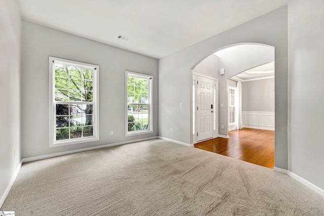 carpeted empty room with arched walkways, visible vents, and baseboards