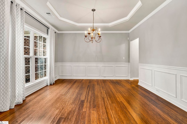 unfurnished dining area featuring a chandelier, a tray ceiling, visible vents, wainscoting, and wood finished floors