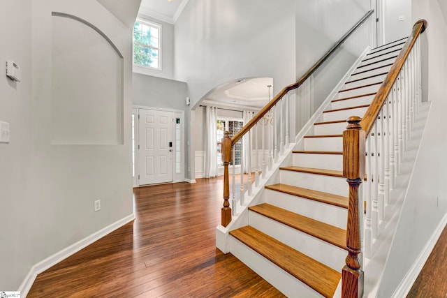 foyer featuring crown molding, arched walkways, a towering ceiling, wood finished floors, and stairs