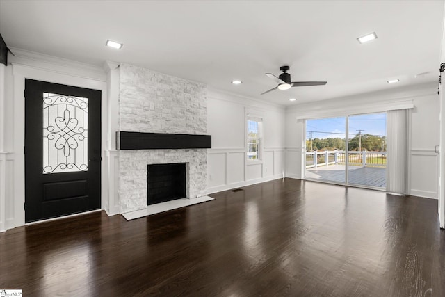 unfurnished living room with ornamental molding, a ceiling fan, a stone fireplace, and wood finished floors