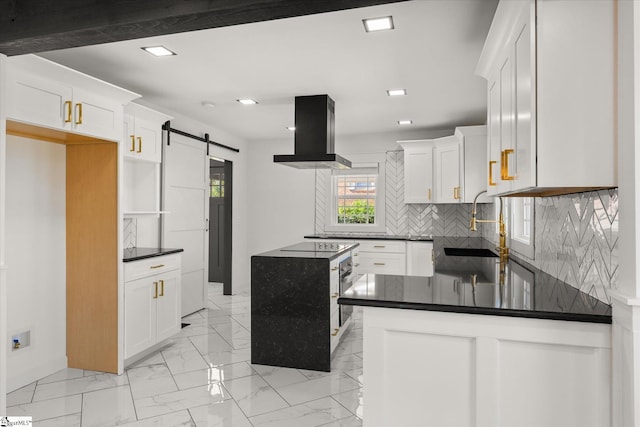 kitchen featuring a sink, a barn door, tasteful backsplash, dark countertops, and island range hood