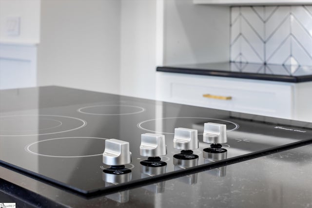 room details featuring black electric cooktop, white cabinets, and dark stone counters