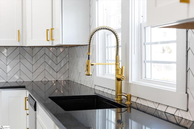 kitchen with dark stone countertops, decorative backsplash, white dishwasher, a sink, and white cabinetry