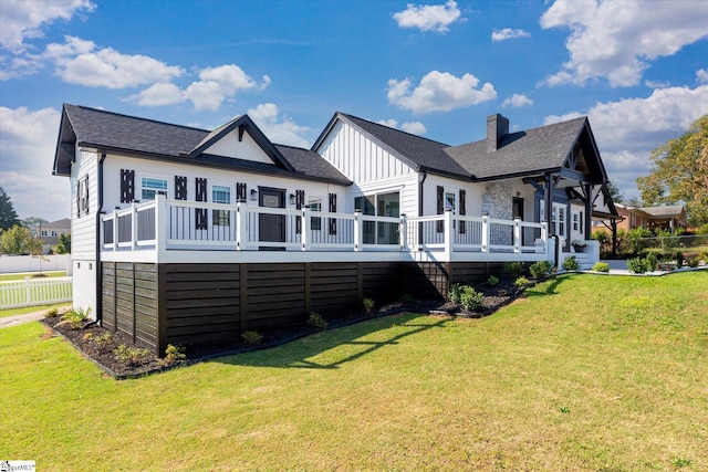 back of property with a wooden deck, a shingled roof, a lawn, board and batten siding, and a chimney