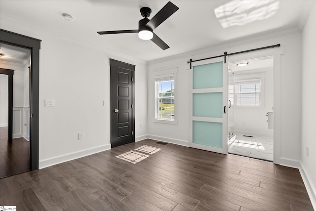 unfurnished bedroom with visible vents, a barn door, ornamental molding, and dark wood-style flooring
