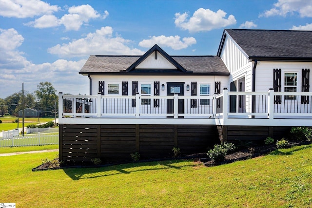 rear view of house with a deck, board and batten siding, a shingled roof, and a yard