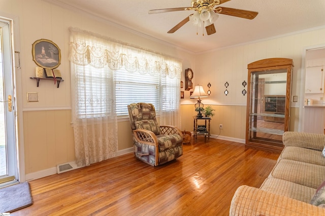 living room featuring crown molding, a ceiling fan, visible vents, and wood finished floors