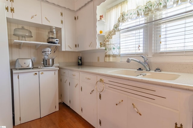 kitchen featuring open shelves, a sink, light countertops, white cabinets, and light wood finished floors