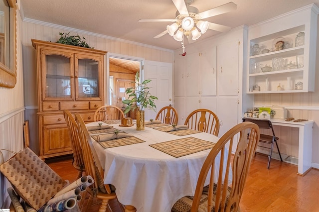 dining space featuring crown molding, a ceiling fan, wooden walls, and light wood-style flooring