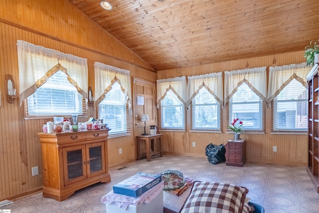 living area with baseboards, wood walls, a wealth of natural light, and vaulted ceiling