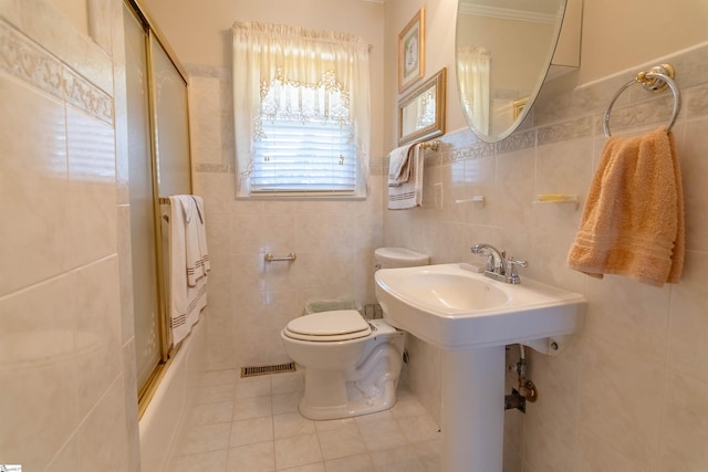 full bathroom featuring tile patterned flooring, toilet, tile walls, visible vents, and bath / shower combo with glass door