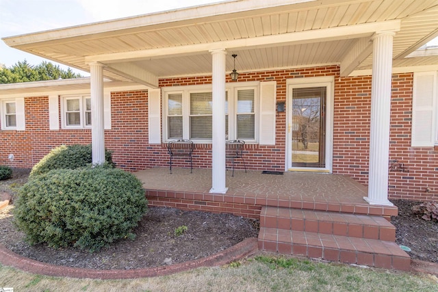 view of exterior entry featuring covered porch and brick siding