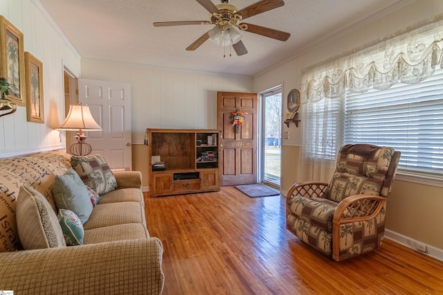 living room with crown molding, a ceiling fan, and light wood finished floors