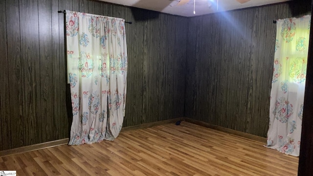 empty room featuring wood finished floors, ceiling fan, and wooden walls