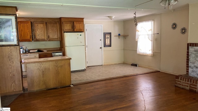 kitchen with wood finished floors, freestanding refrigerator, brown cabinets, baseboards, and dishwashing machine
